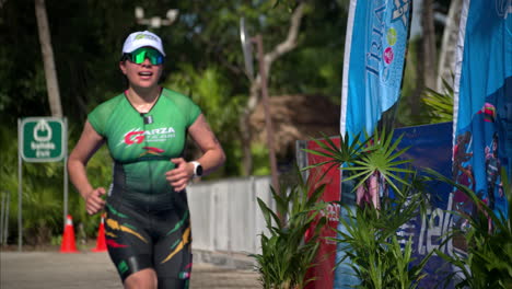 Slow-motion-of-a-female-athlete-in-a-green-suit-jogging-towards-the-finish-line-celebrating-with-her-arms-up