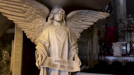 Slow-pan-around-life-size-marble-statue-of-an-angel-in-Candelária-church-with-a-text-written-in-Latin-on-a-banner-in-hands-in-front-of-the-altar