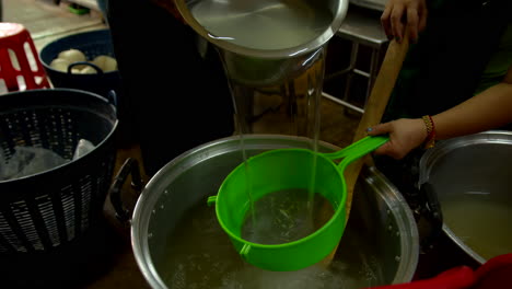 Thailand,-Bangkok---13-August-2022:-Close-up-on-coconut-water-emptied-from-a-pot-and-filtered-with-a-strainer-in-a-cauldron,-ready-to-become-jelly-for-coco-jelly