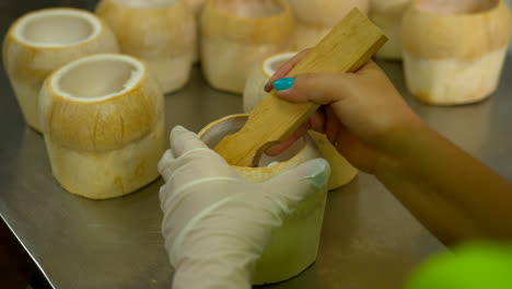 Thailand,-Bangkok---13-August-2022:-Close-up-unidentifiable-worker-preparing-the-shell-for-coco-jelly,-famous-thai-street-food,-extracting-coconut-pulp-using-scraper