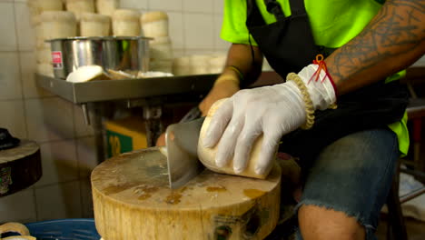 Thailand,-Bangkok---13-August-2022:-Unidentifiable-worker-cutting-bottom-and-top-of-fresh-peeled-green-coconut-preparing-shell-for-coco-jelly,-famous-thai-dessert