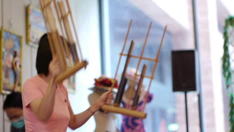 Bamboo-Angklung-being-shaken-by-Asian-woman-wearing-face-mask-dancing-around-happily,-filmed-in-handheld-style-as-medium-close-up