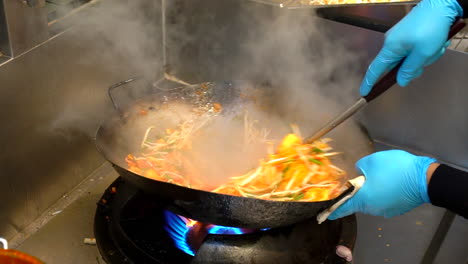 Thailand,-Bangkok---18-August-2022:-Unrecognizable-chef-adding-veggie-and-sauce-to-pad-thai-noodles-stir-frying-on-hot-wok-pan-in-restaurant