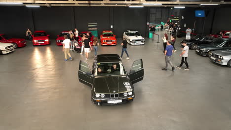 Shiny-black-BMW-e30-classic-car-parked-in-warehouse-club-bar-show-showcase,-orbiting-aerial-view