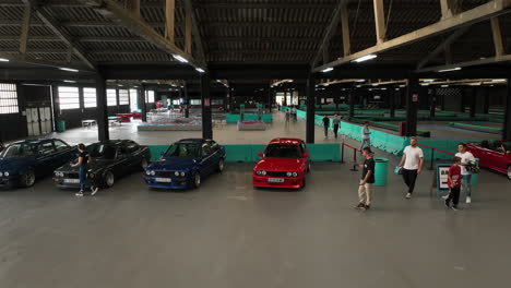 Person-cleans-BMW-e30-at-indoor-show,-vintage-cars-in-bright-colors,-aerial