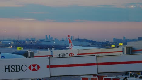 Hsbc-Ladebrücken-Führen-Am-Frühen-Morgen-Zu-Flugzeugen-Mit-Dem-Stadtbild-In-Der-Ferne