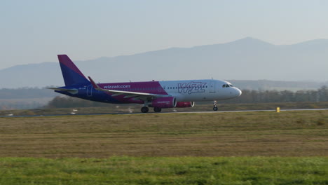 Toma-De-Seguimiento-Del-Avión-Wizz-Air-Despegando-En-El-Aeropuerto-De-Sibiu-En-Un-Día-Soleado,-Rumania