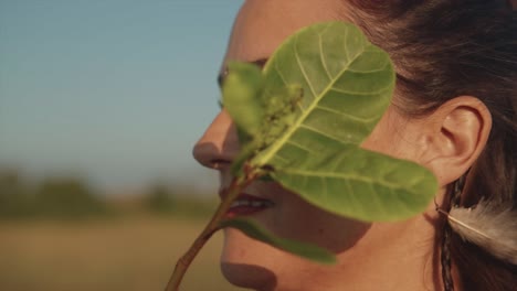 Beautiful-portrait-of-a-brunette-Indian-woman-hiding-her-face-with-a-green-leaf,-smiling-softly