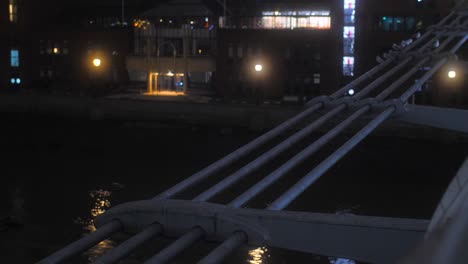 Close-up-shot-of-side-details-of-Millennium-bridge-with-the-view-of-Thames-river-below-in-London,-England,-UK-at-night-time