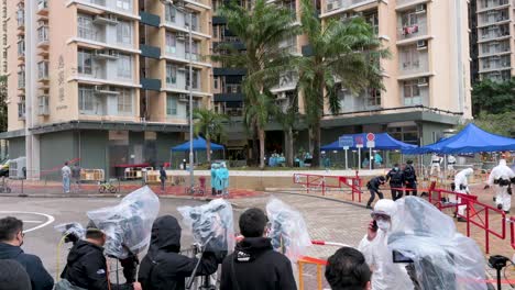 Los-Miembros-De-La-Prensa-Se-Paran-Frente-A-Un-Edificio-Residencial-Cerrado-Mientras-Filman-A-Los-Trabajadores-De-La-Salud-Y-A-Los-Policías-Que-Pasan-Junto-A-Ellos-Después-De-Que-Una-Gran-Cantidad-De-Residentes-Dieron-Positivo-En-Hong-Kong