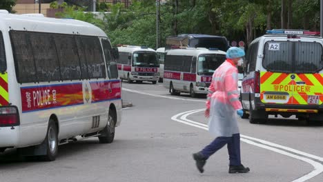 Ein-Polizist,-Der-Einen-Psa-anzug-Trägt,-Geht-über-Den-Rahmen,-Während-Polizeiwagen-Vor-Einem-Wohngebäudekomplex-Unter-Covid-19-coronavirus-sperrung-Geparkt-Sind