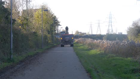 Vista-Trasera-De-Una-Excavadora-Conduciendo-Por-Un-Camino-Estrecho-A-Través-Del-Campo-En-Dublín,-Irlanda