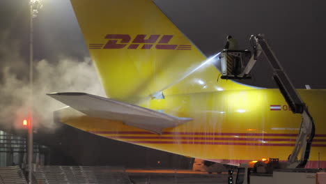 Heck-Und-Höhenruder-Eines-Dhl-frachtflugzeugs,-Das-In-Einer-Kalten-Winternacht-Einer-Enteisungsbehandlung-Unterzogen-Wird