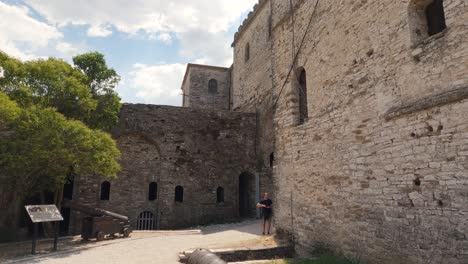 Touristen-Gehen-Vorbei,-Während-Die-Kamera-Von-Den-Historischen-Festungsmauern-Zum-Kanon-Der-Burg-Gjirokaster-Schwenkt