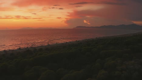 Hermosas-Imágenes-Aéreas-De-Drones-De-Cine-Anamórfico-Del-Bosque-De-Pinos-Y-La-Playa-De-Arena-Junto-Al-Mar-En-El-Icónico-Parque-Natural-Maremma-En-Toscana,-Italia-Con-Nubes-Dramáticas-Que-Cubren-El-Cielo-Al-Atardecer