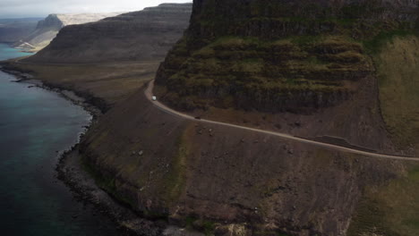 Vehicles-driving-on-narrow-path-on-cliff-in-Iceland,-drone-shot