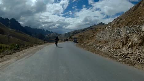 View-Of-Biker-Travelling-On-The-Mountain-Road-To-Leh-In-Ladakh,-India-On-A-Sunny-Day---rolling-shot