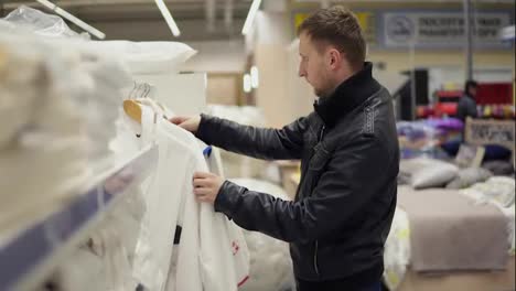 Young-man-in-a-leather-jacket-chooses-a-bathrobe-in-the-store-of-bed-linen-and-accessories