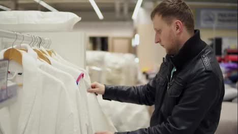 Closeup-view-of-a-young-man-in-a-leather-jacket-chooses-a-bathrobe-in-the-store-of-bed-linen-and-accessories