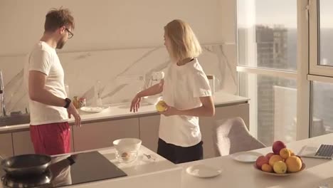 Beautiful-young-caucasian-man-preparing-breakfast-for-two-in-kitchen-at-home-and-mixing-eggs-in-bowl,-wife-coming-over-and-kiss