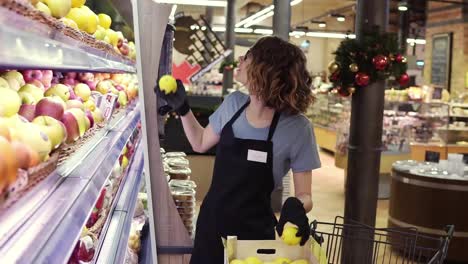 Seitenansicht-Einer-Hübschen-Kaukasischen-Arbeiterin-In-Schwarzer-Schürze-Und-Handschuhen,-Die-Die-Früchte-Im-Supermarkt-Einlagert.-Junger-Mitarbeiter-Bei-Der-Arbeit.-Lockig