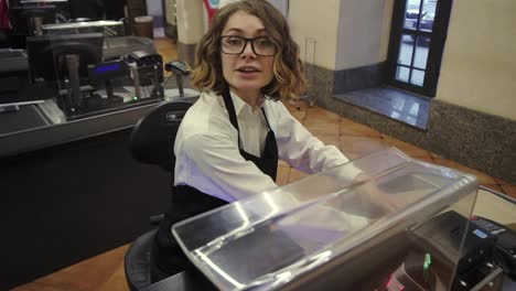 Cheerful-caucasian-saleswoman-in-white-shirt-and-black-apron-scanning-product,-fruits-at-checkout-counter-in-bright-supermarket