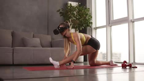 Sportive-girl-with-perfect-muscular-body-wears-VR-mask-during-her-home-work-out-at-living-room.-Girl-in-a-mask-doing-legs