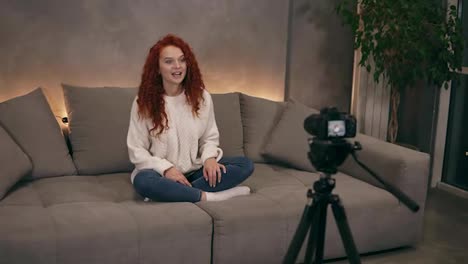 Attractive-curly-redhead-young-girl-vlogger-is-talking-in-front-of-camera-recording-video-for-online-blog-in-internet