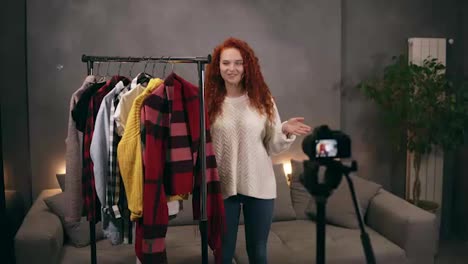 Stylish-redhead-young-woman-vlogger-is-recording-video-for-online-blog-about-trendy-clothes-standing-nextto-the-rack-with