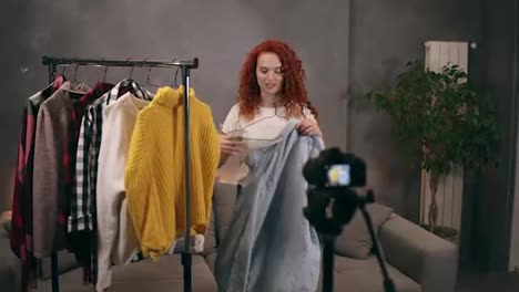 Estilista-Femenina-Grabando-Un-Video-Para-Un-Blog-En-Línea-Mostrando-Ropa-De-Moda,-Hablando-Y-Gesticulando-Con-La-Cámara.-Chica-Probándose-Ropa.