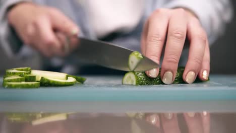 Front-view-of-woman's-hands-slicing-fresh-cucumber-on-cutting-board-in-slow-motion.-Close-up-of-woman's-hands-with-beige