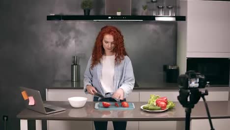 Young-woman-in-casual-clothes-leads-a-culinary-blog-and-records-video-in-grey-kitchen.-Video-shooting-of-the-blog---redhead