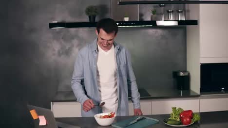 Super-excited-young-man-holding-spoon-as-a-microphone-singing-songs-and-dancing-while-cooking-in-kitchen,-carefree-man-preparing