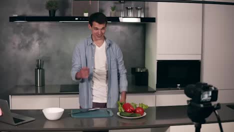 Young-man-in-casual-clothes-leads-a-culinary-blog-and-records-video-in-grey-kitchen.-Video-shooting-of-the-blog---welcomes-his