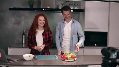 Young-couple-in-casual-cooking-together-and-recording-video-food-blog-on-camera-in-the-loft,-grey-kitchen-at-home.-Excited