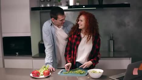 Pareja-Divertida-Cocinando-Juntos-En-Una-Cocina-De-Color-Gris,-Familia-Joven-Y-Activa-Divirtiéndose,-Riendo-Y-Sin-Preocupaciones.-Hombre-Feliz