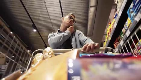 At-the-Supermarket:-Busy-man-in-glasses-with-shopping-cart-uses-smartphone---talking.-Looks-at-dairy-products-and-walks-through