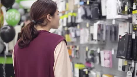 Imágenes-De-La-Parte-Trasera-De-Una-Chica-Morena-Tomando-Una-Caja-Con-Auriculares-De-La-Exhibición-En-Una-Tienda-De-Electrónica