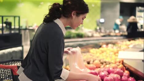 Young-beautiful-brunette-girl-in-her-20's-picking-out-tangerines-into-a-plastic-bag-at-the-fruit-and-vegetable-aisle-in-a