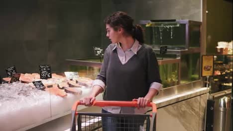 Young-female-customer-trying-to-choose-what-fish-to-buy-looking-at-and-touching-price-tags-in-a-supermarket