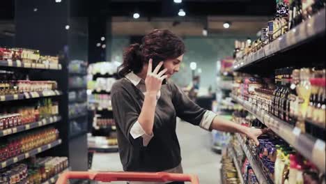 Beautiful-female-buyer-trying-to-choose-products-at-grocery-store-while-speaking-with-someone-on-the-phone