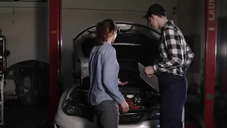 Cute-car-or-automotive-technician-wearing-work-robe-and-a-cap-is-meeting-with-his-female-clients-and-hears-out-complaints-about