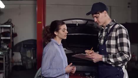 Young-attractive-female-car-owner-explains-to-automotive-technician-all-her-complains-about-her-vehicle-and-signes-something-on