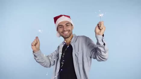 Happy-New-Year-Cheerful-young-caucasian-man-in-casual-clothes-and-santa-hat-holding-two-sparklers,-waving-them-in-a-rhythm-and