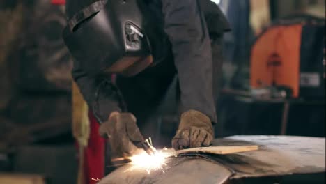 Unrecognizable-worker-with-welding-helmet-on-cuts-off-metal-piece-with-a-oxy-acetylene-cutting-torch-at-a-mechanical-hangar