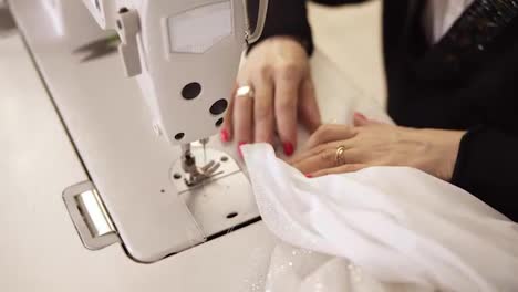 High-angle-view-of-female-hands-with-colored-manicure-in-process-of-creating-wedding-white-dress.-Clothes-designer-working-with