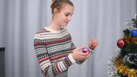 Attractive-happy-woman-in-christmas-sweater-smiling-and-decorating-a-Christmas-tree-with-toys-in-her-apartment.-shot-in-4k