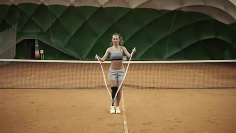 Atleta-Femenina-Atractiva-Saltando-La-Cuerda-En-Una-Cancha-De-Tenis-Cubierta.-Hándicap.-Vista-Frontal.-Cámara-Lenta.