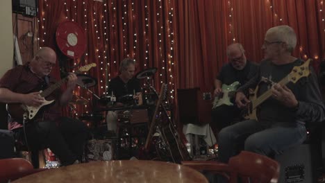 Band-of-elderly-men-playing,-jamming-in-a-bar-retirement-hobby-music-with-guitars-and-drums-in-4k
