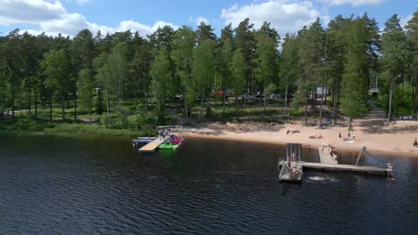 People-play-and-jump-off-of-dock-swimming-in-alpine-lake-below-forest-in-Sweden